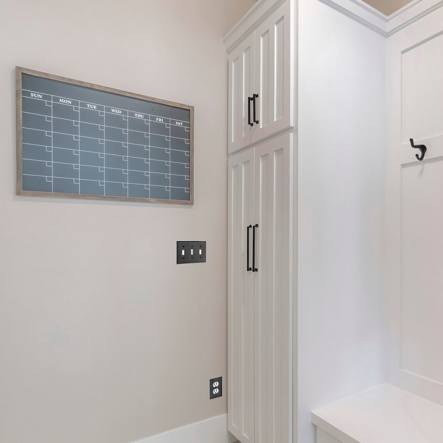 white mudroom coat closet organization with black metal coathooks switch plate and cabinet hardware