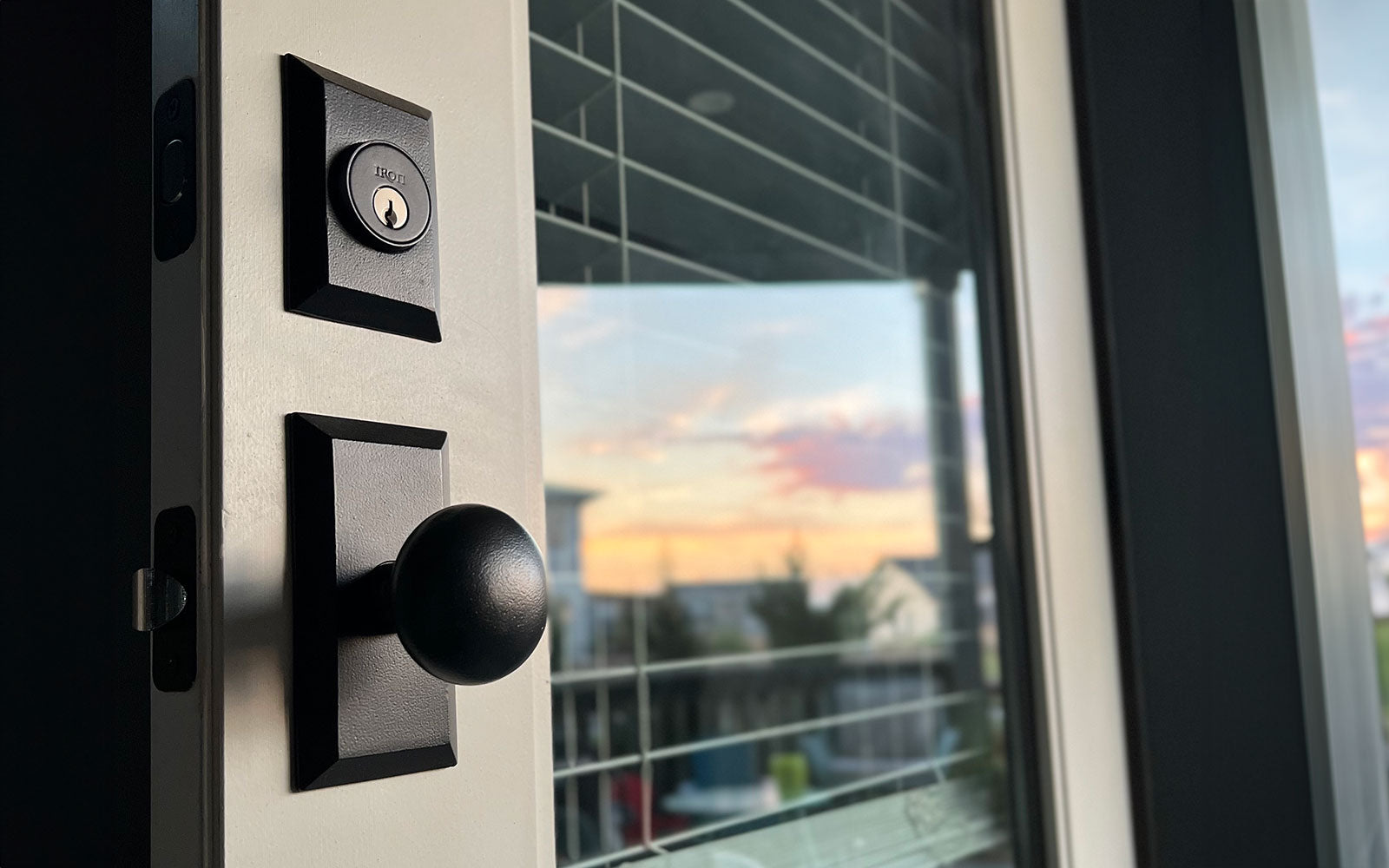 Black matte cast iron entry handleset and deadbolt on a front door at sunset